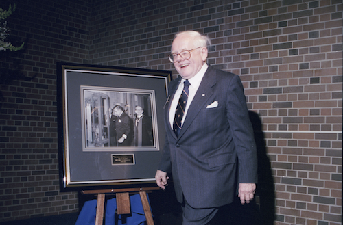 President Doug Wright at his farewell event next to a photo of himself as Dean of Engineering.