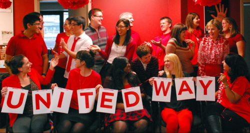 Co-workers wearing read gather for a group photo holding signs that spell out United Way.