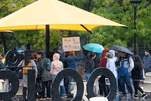 Protestors holding signs and umbrellas on the Arts Quad.