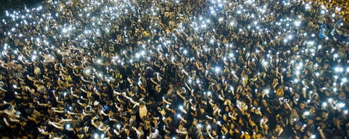 Thousands of people hold cell phones up during a public demonstration.