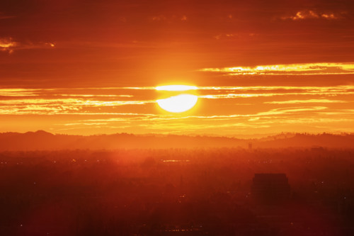 The sun hangs heavily in an orange-clouded sky over a sweltering cityscape.