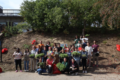 Students and other volunteers holding plants in front of the embankment.
