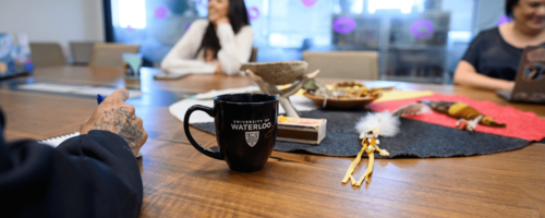 People sit around a meeting table with Indigenous cultural items in the centre.