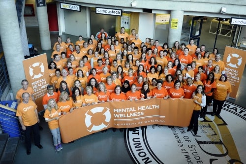 Volunteers wear orange shirts and pose with a mental health banner.