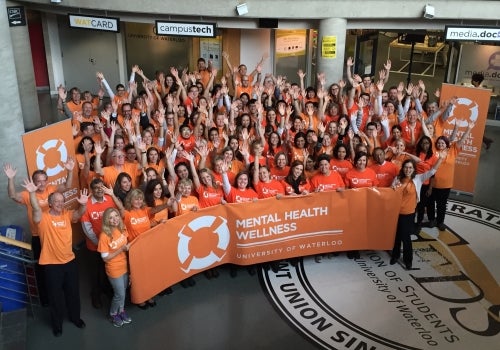 Participants in Mental Health Wellness Day hold up orange banners.