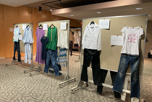 The What Were You Wearing exhibit in the SLC Multipurpose room, showing displays of clothing with testimonials.