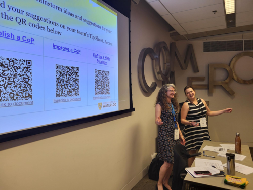 Nancy Goucher and Nadine Quehl stand next to a projection screen while they give a presentation.