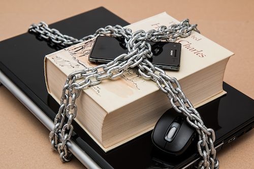 A laptop, hardcover book and smartphone locked together with heavy chains.