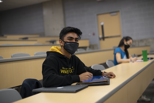Masked students studying in a lecture hall.