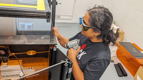 A student wears eye protection as they interact with laser lab equipment.