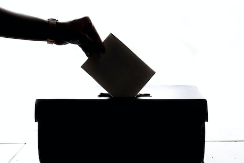 A silhouette of a person placing a ballot in a ballot box.