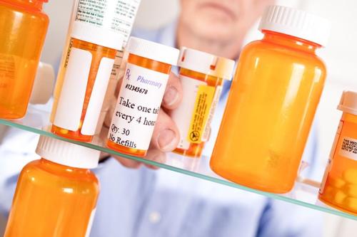 A pharmacist picks up a bottle of medication from a shelf filled with similar bottles.
