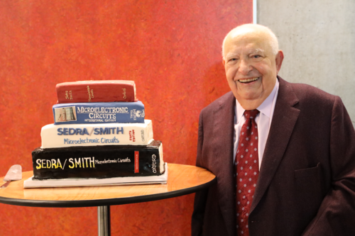 Dr. Adel Sedra stands next to a cake shaped like a stack of his textbooks.