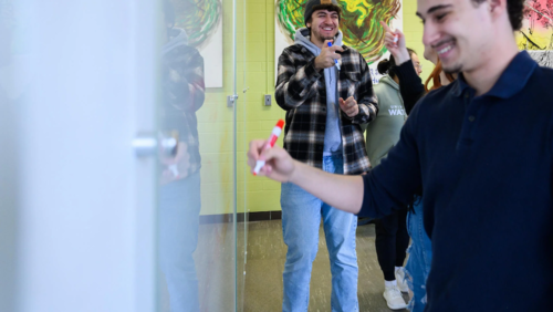 Students laugh as they use markers on a whiteboard.