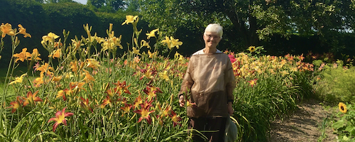 Wendy Mitchinson stands next to some flowers on a trail.