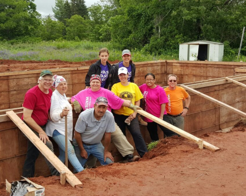 Members of the UWaterloo Habitat for Humanity Build Team pose in front of a foundation.