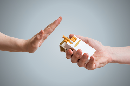 A person holds up a hand to stop another from offering a cigarette from a pack.
