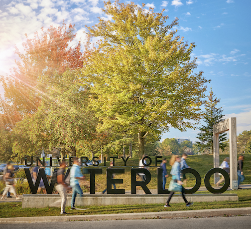 Students walk past the University of Waterloo sign in autumn.