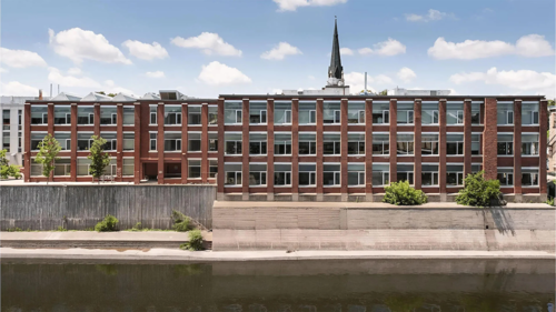 L'extérieur du Riverside Silk Mill abritant l'école d'architecture de Cambridge avec un clocher d'église en arrière-plan.