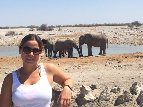 Ibi Brown poses with elephants at a watering hole in the background.