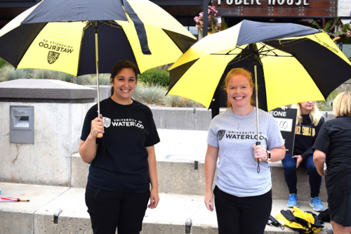 Two volunteers in Waterloo shirts hold umbrellas during the annual Umbrella March fundraising event.