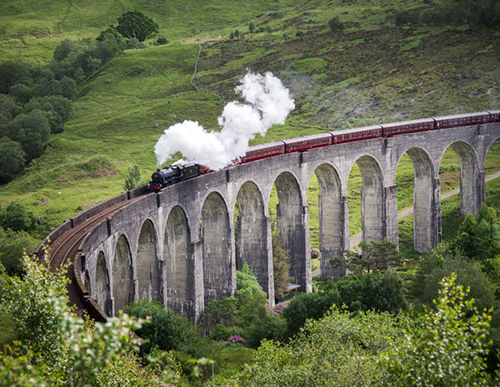 A steam train travels over a stone bridge.