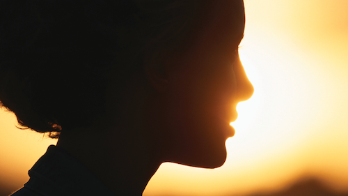 A woman's face in silhouette with the setting sun behind.