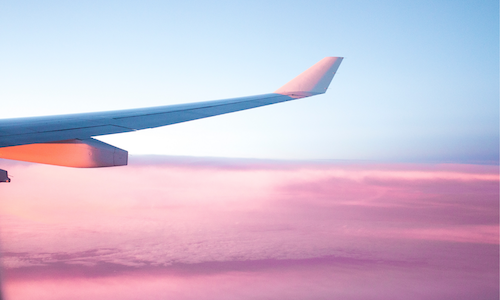 A photo of an airplane's wing with pink clouds beneath it.