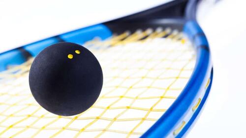 A close-up image of a squash ball balacing on a racket.