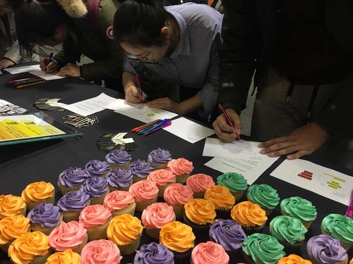 Students signing postcards in front of an array of cupcakes with coloured frosting.
