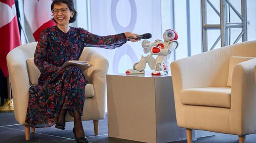 Pearl Sullivan laughs as she holds a microphone up to a robot's mouth.