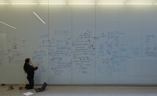 A woman writes equations on a long whiteboard.