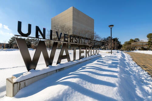 The University of Waterloo sign with the Dana Porter Library in the background in a winter setting.
