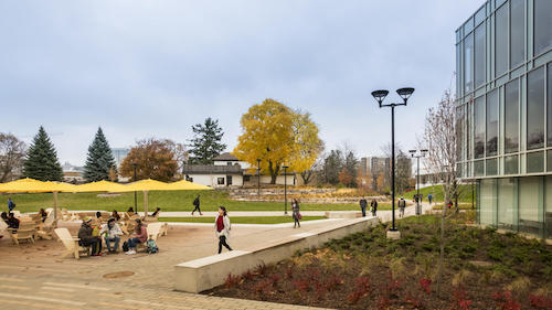 Students sit at patio tables on the Arts Quad with the Grad House in the background.