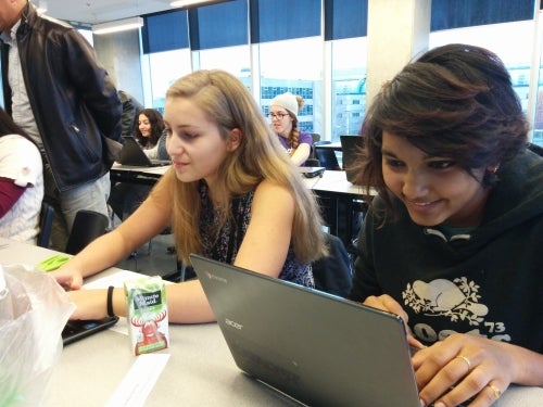 Young women work at laptops at the Code Squad event.