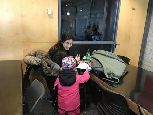 A preschooler hands a Waterloo student a holiday card in the Student Life Centre.