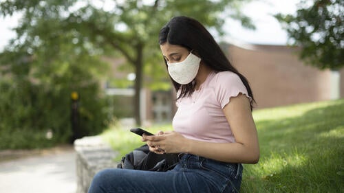 A woman wearing a mask looks at her smartphone.