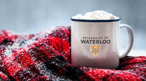 A University of Waterloo mug brimming with hot cocoa surrounded by a red and black flannel scarf.