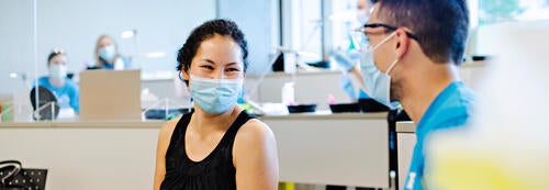 A masked person smiles at a health care worker.