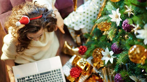 A woman reads a laptop next to a Christmas tree.