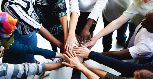 A diverse group of people put their hands in for a diversity cheer.