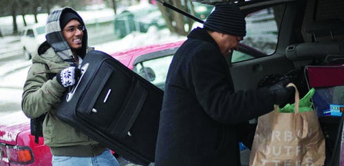 Two students load suitcases into the trunk of a car