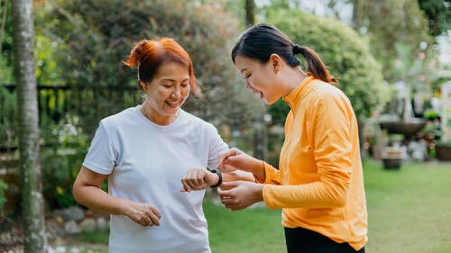 Two women consult one's wearable device while out jogging.