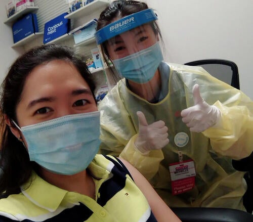 Woman in PPE gives two thumbs up after giving another woman a vaccination