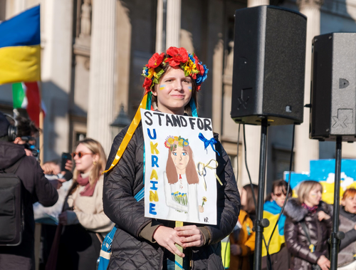 A woman holding a &quot;Stand with Ukraine&quot; sign.