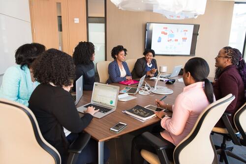 Black women with various devices seated at a boardroom table.