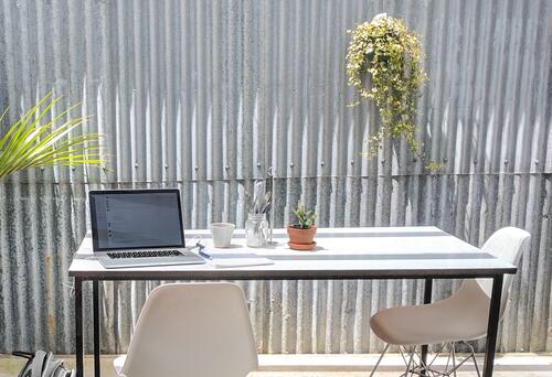 Desk with a lap and plant on it in front of an aluminium sided wall