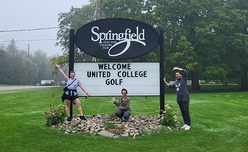 The golf tournament organizing committee; Reid McRob, Rebecca Wagner, and Rubin Kataki pose in front of Springfield Golf Course sign and point at United College Golf Tourney placard.