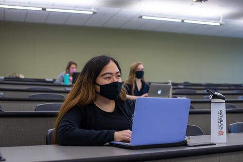 Students wearing masks sit apart from one another in a lecture hall.