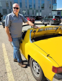 Michael Herz stands next to a vintage yellow convertible.